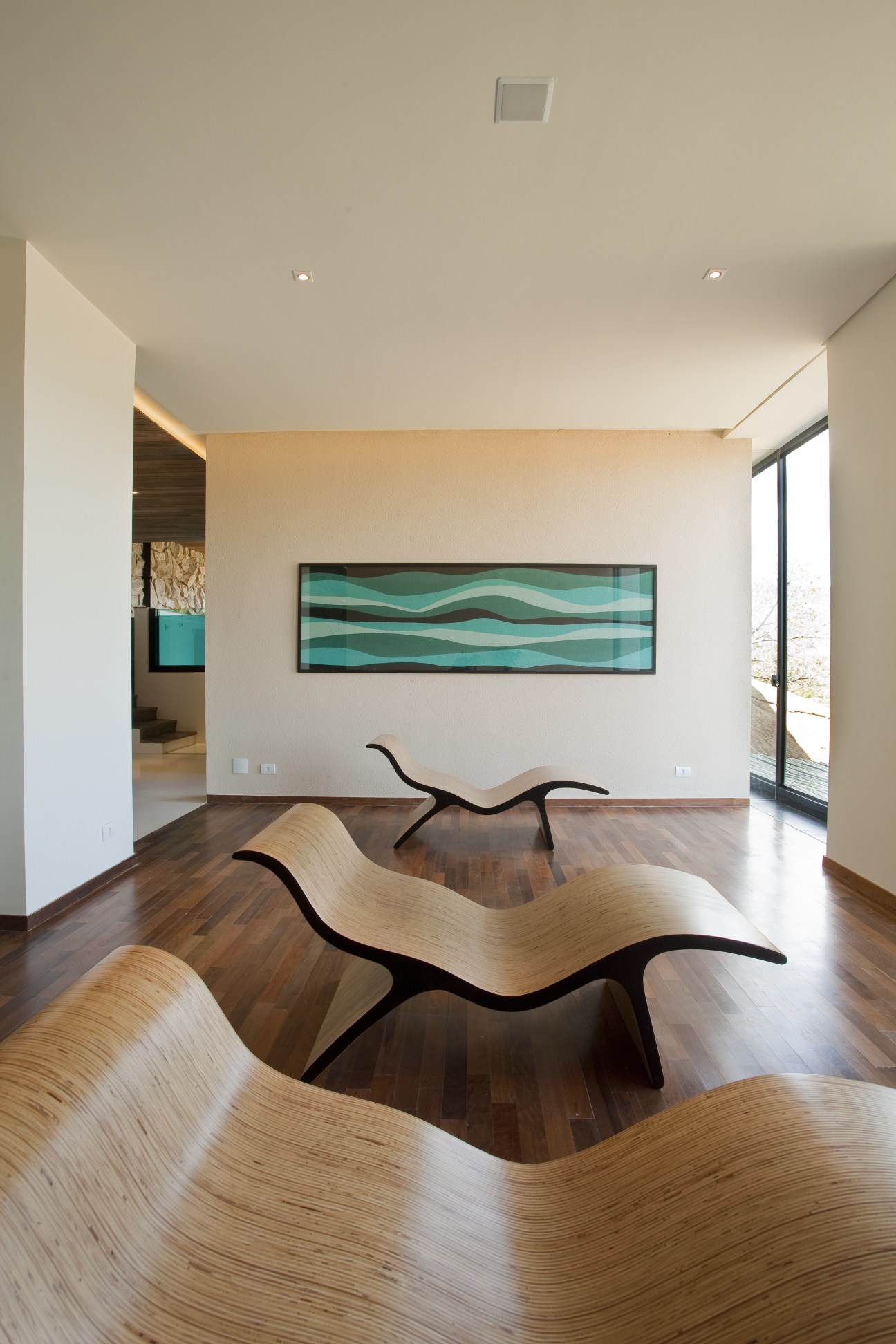 Modern interior with curved wooden lounge chairs, white walls, turquoise abstract artwork, and dark wood flooring at Botanique Hotel and Spa.