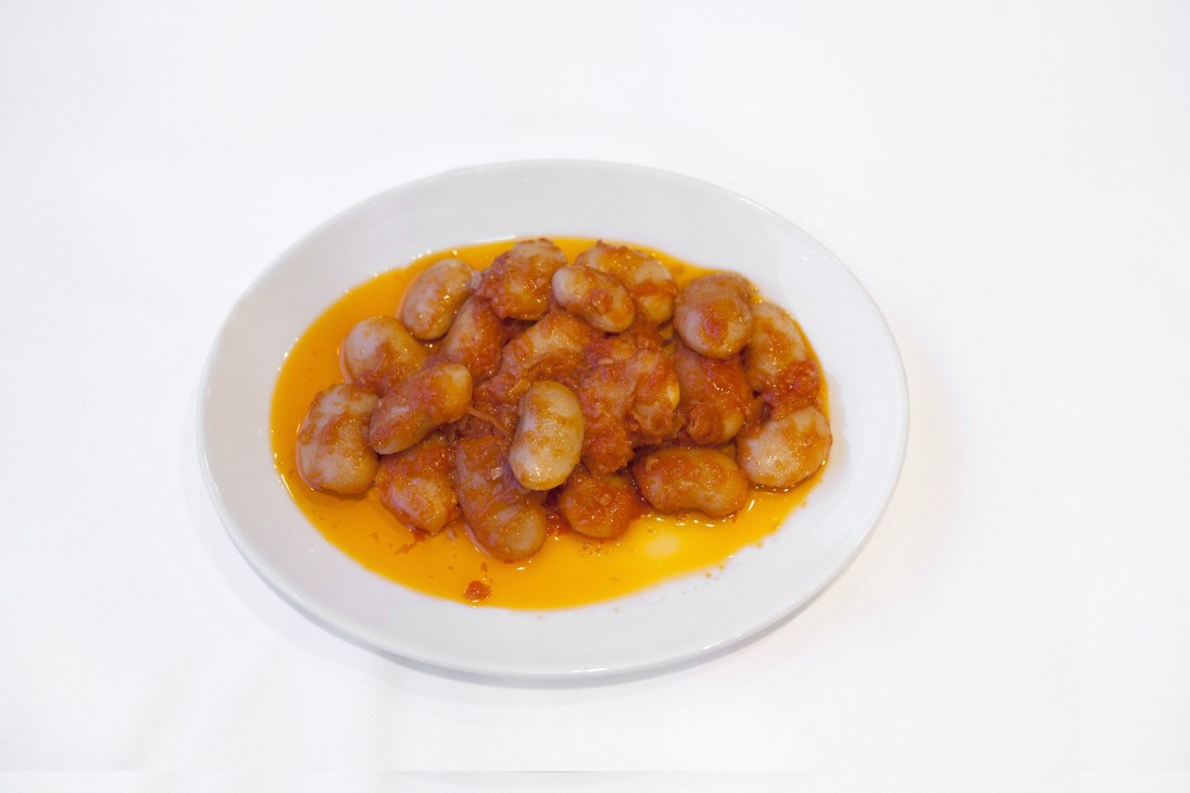 White plate of fasulye pilaki with dried beans in tomato sauce and olive oil