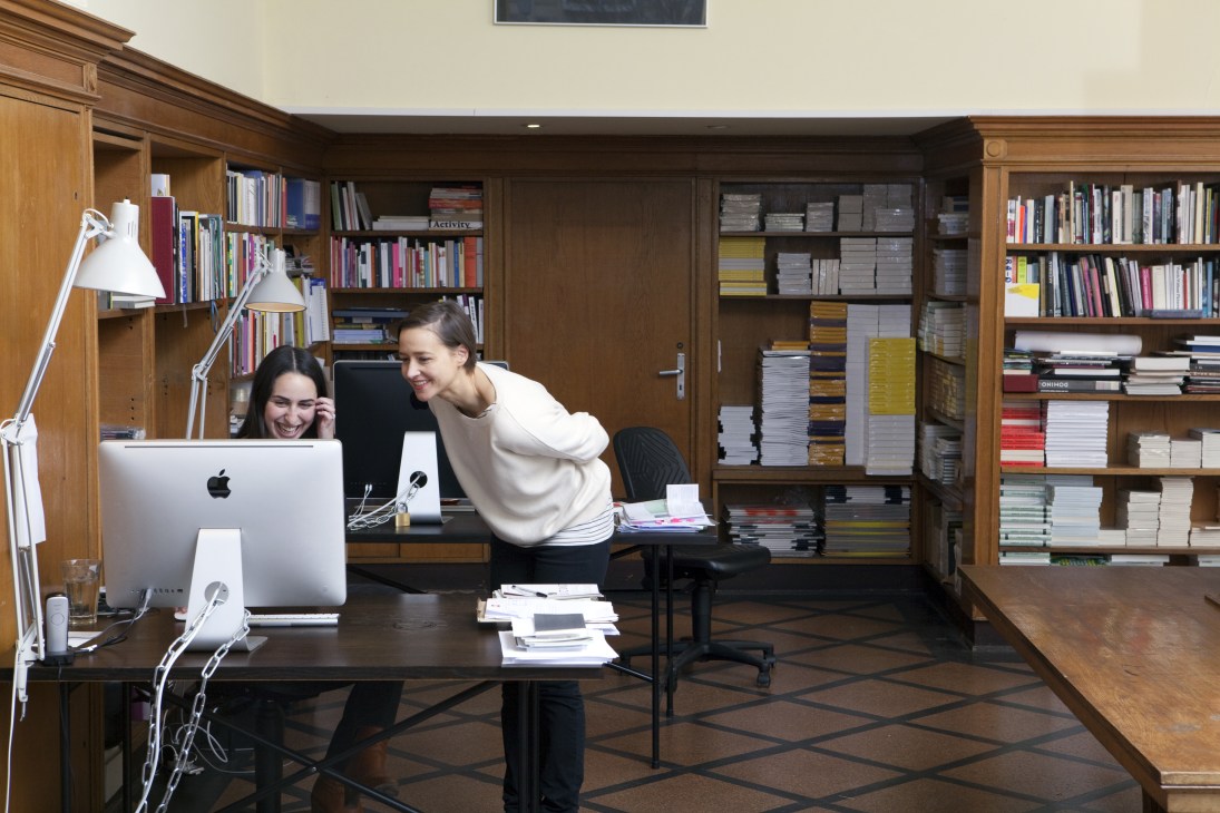 Two women work at a desk in a wood-panelled office lined with bookshelves at Sternberg Press.