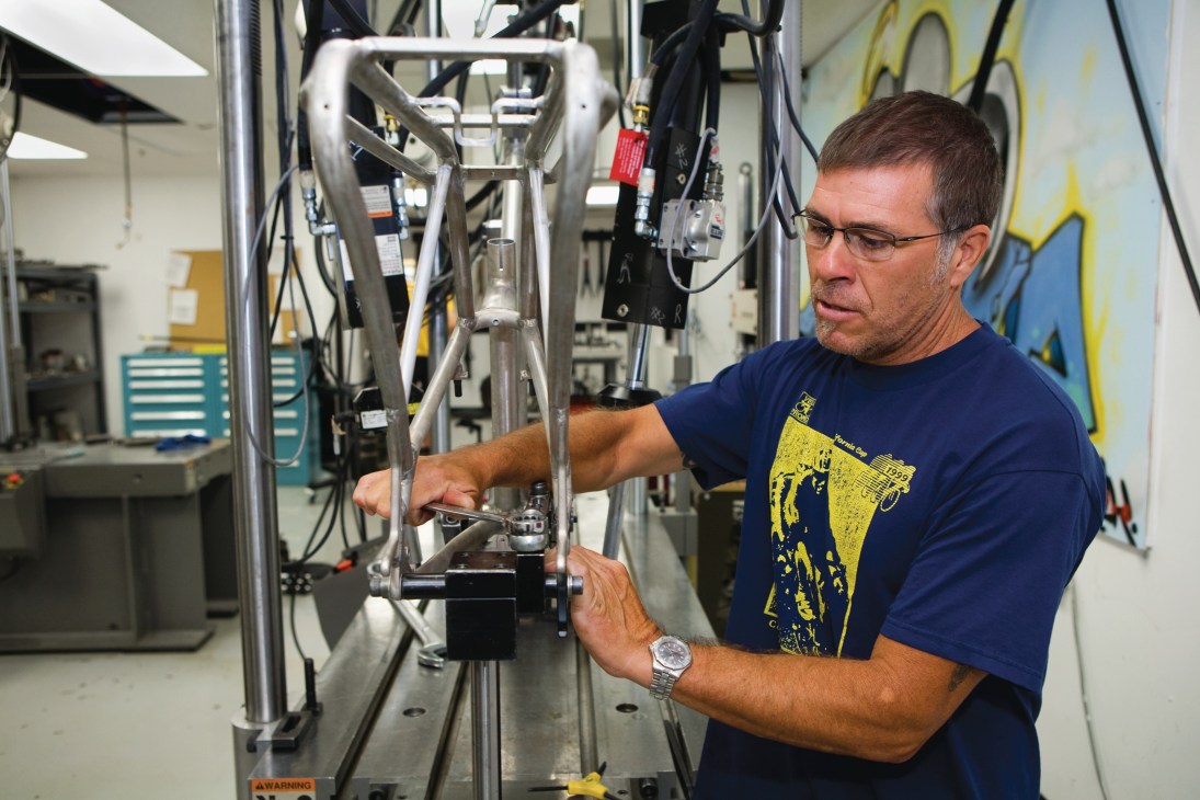 A technician conducts safety testing on a bicycle frame using specialized testing equipment in a workshop.