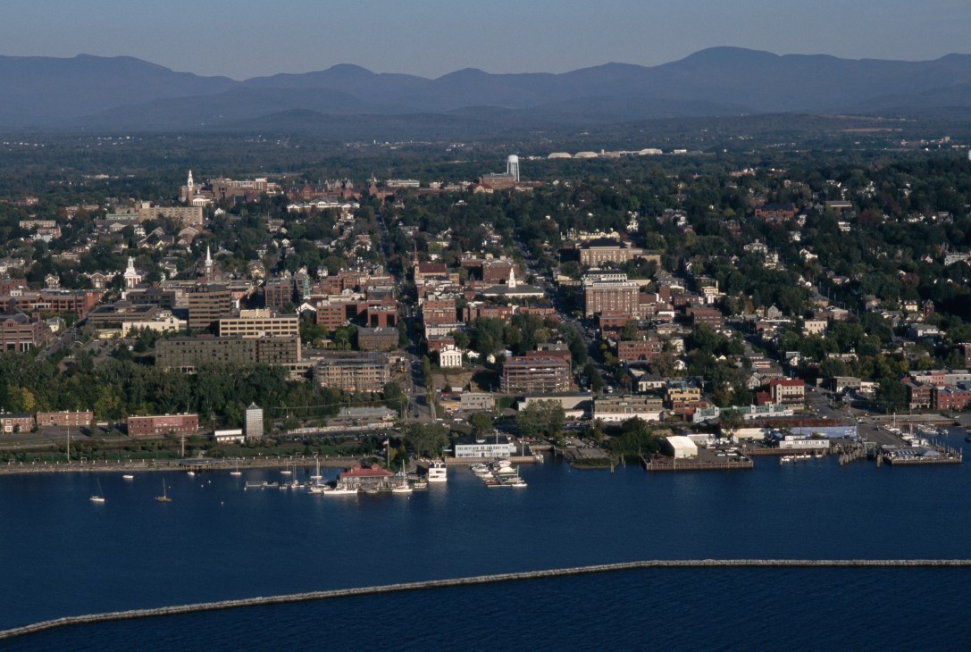 Aerial view of Burlington, Vermont with Lake Champlain in foreground and Adirondack Mountains in background.