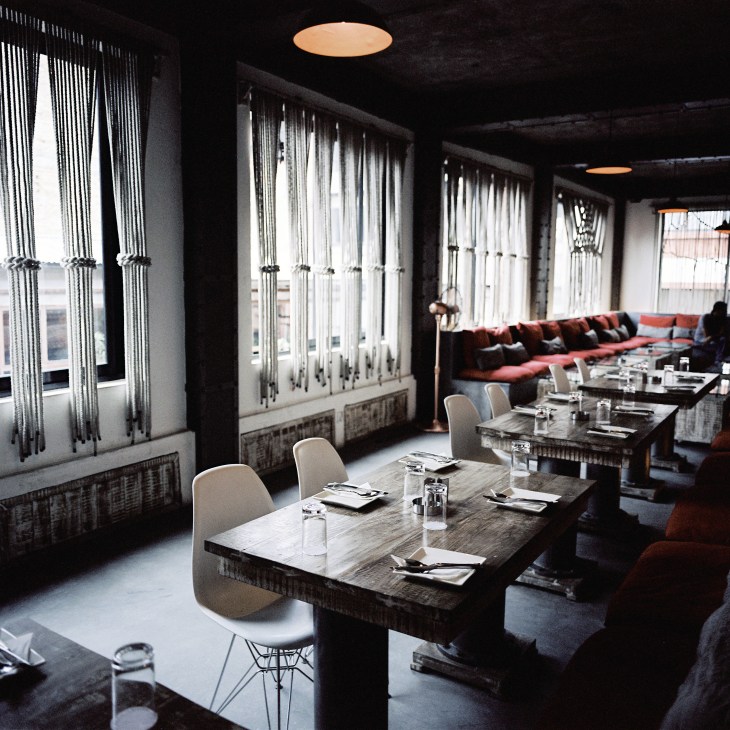 Modern dining tables with white chairs in The Factory restaurant, Kathmandu, with floor-to-ceiling windows and copper ceiling lights.