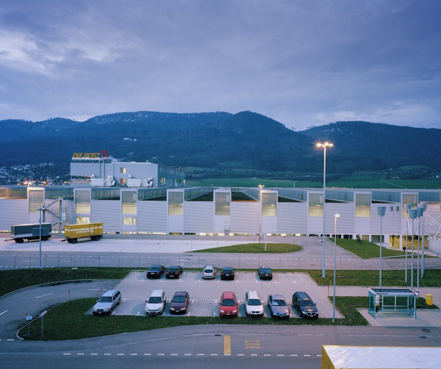 Swiss Post's Härkingen sorting office at dusk with mountains in the background.