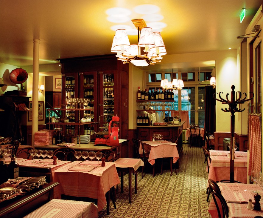 Interior of La Fontaine de Mars restaurant with red tablecloths, wooden wine cabinets, and warm lighting.