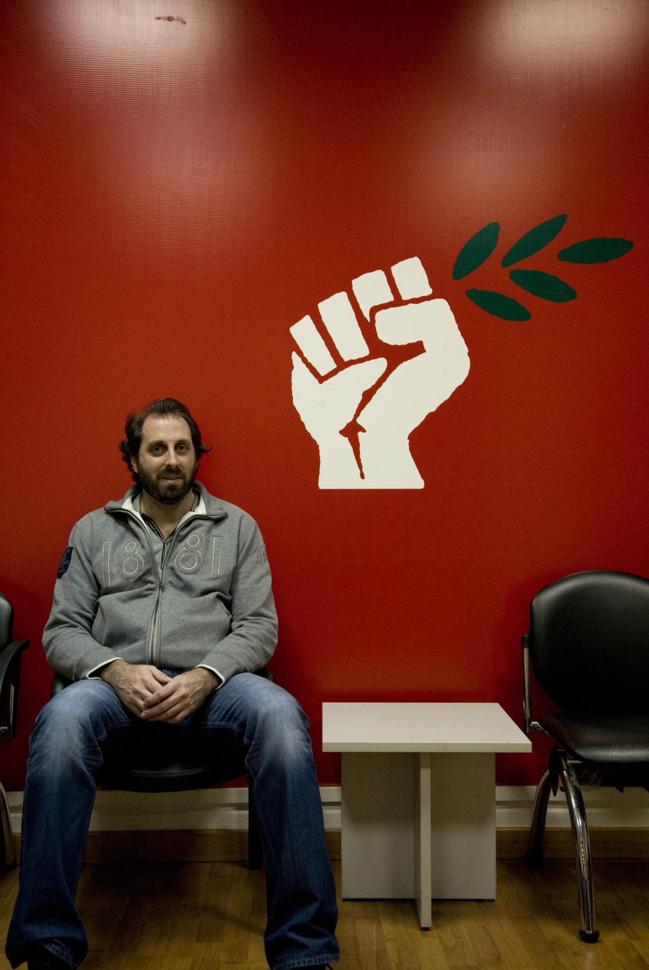 Elie Fawaz from Quantum advertising agency sits before a red wall with a white fist and olive branch March 14 campaign poster.