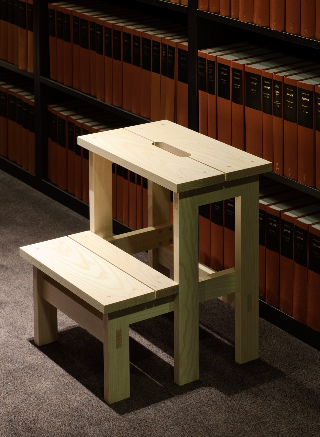 Light wood library stool with stepped design in front of law library shelves.