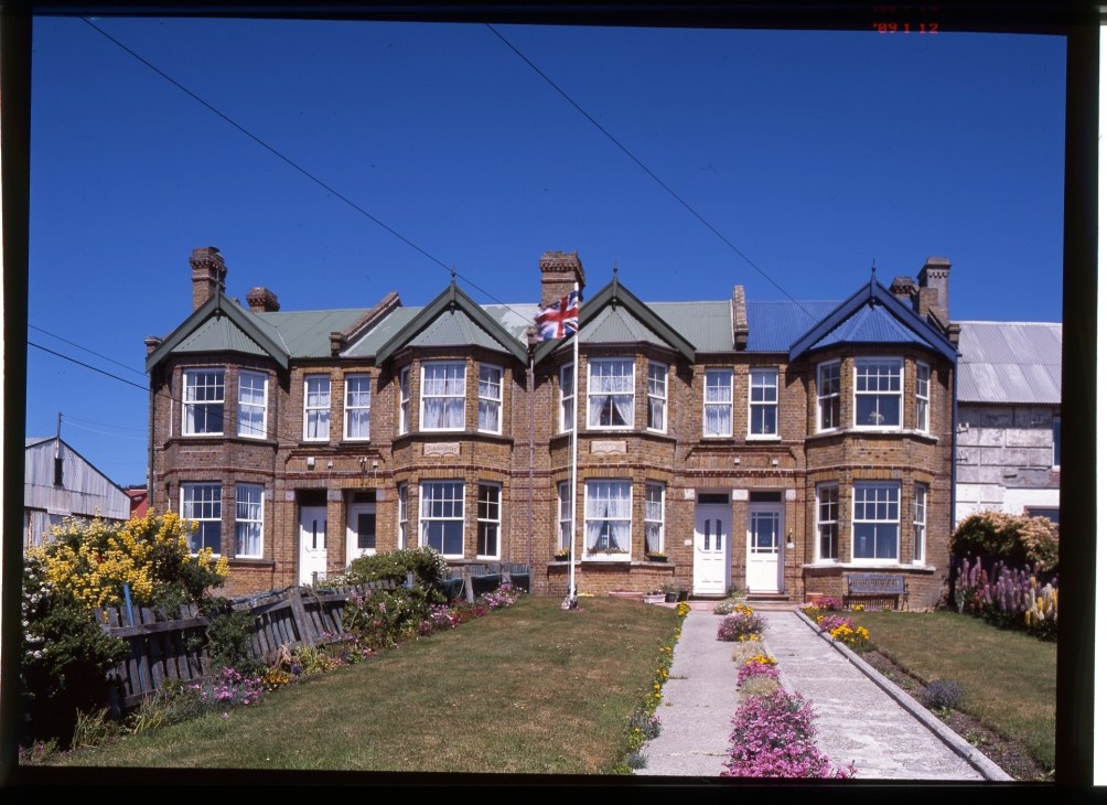 Jubilee Villas, a red brick Victorian building with Union Jack flag flying and colorful gardens in front.