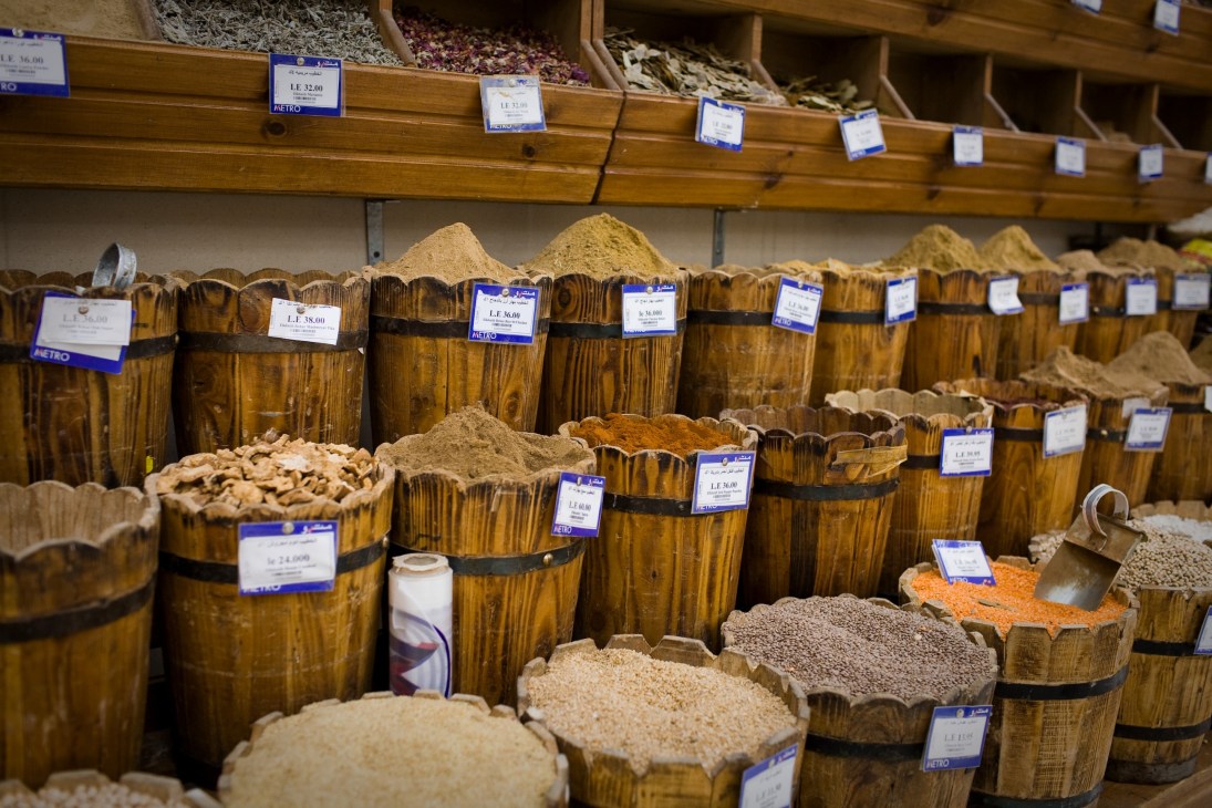 Wooden barrels filled with various spices and herbs with blue price tags at Metro supermarket in El Korba.