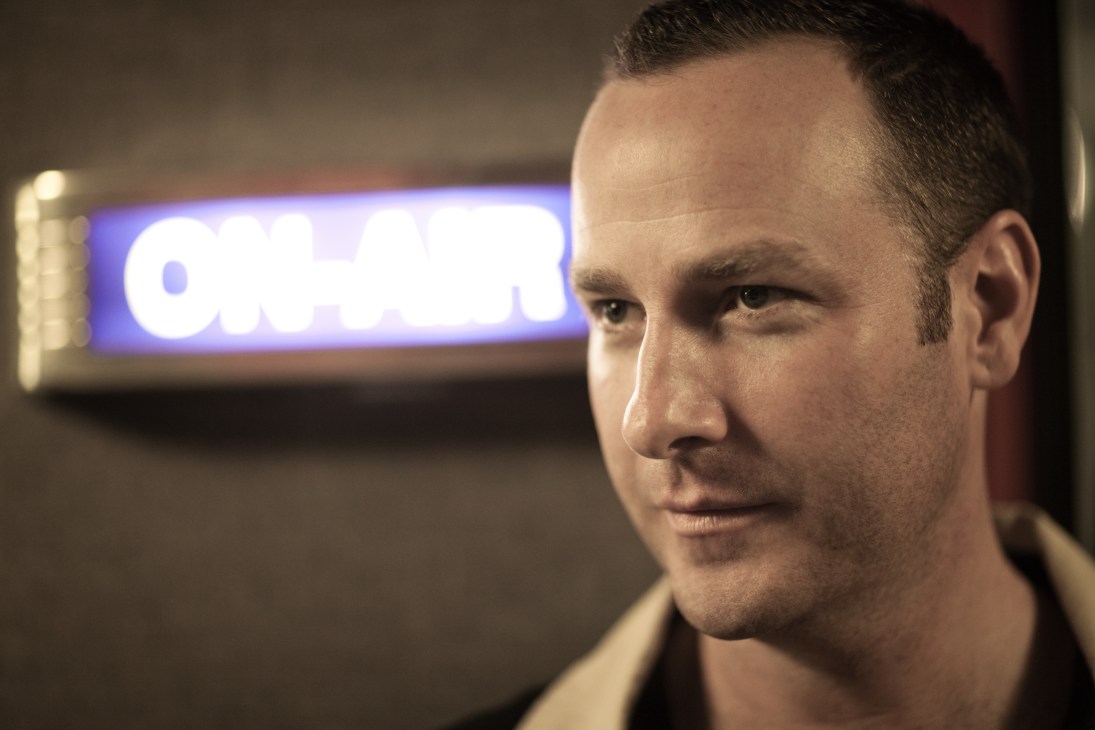 Jason Bentley, KCRW's music director, photographed in profile with a KCRW sign illuminated behind him.