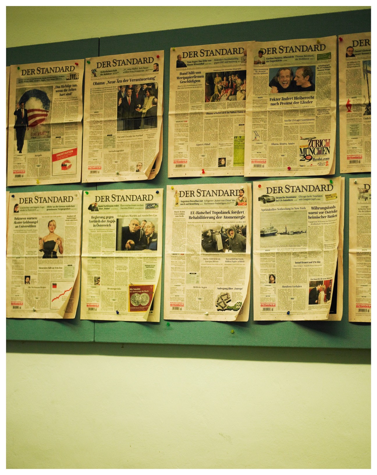 Multiple front pages of Der Standard newspaper pinned to a green wall display.