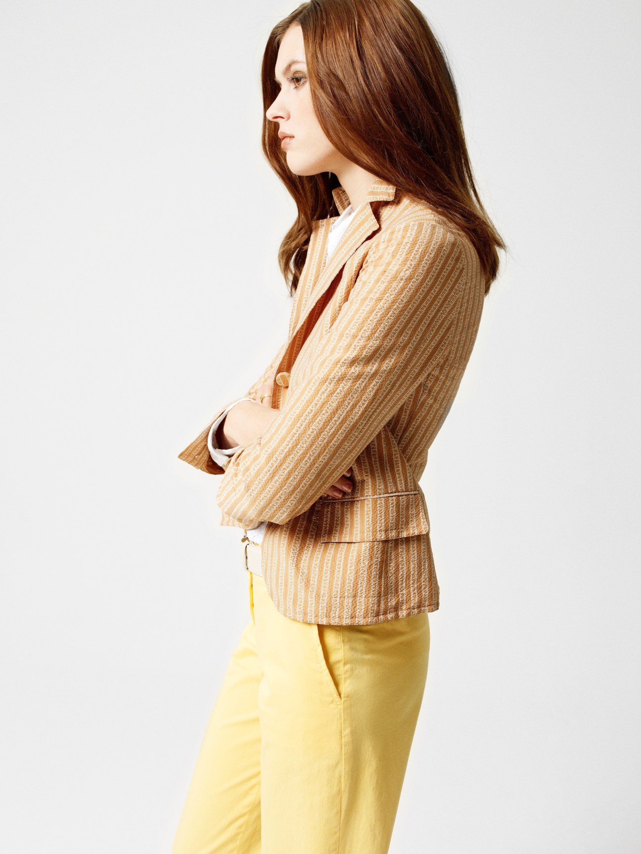 Model wearing a tan striped Bottega Veneta blazer with yellow trousers, side profile against white background.