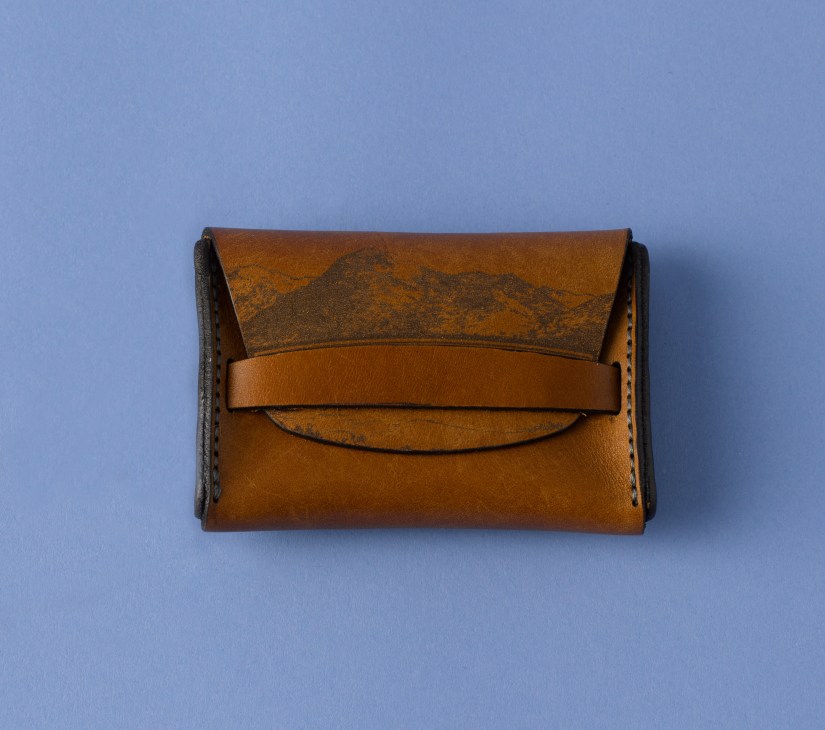 Tan leather wallet with hand-stitched details and a flap closure against a blue background.
