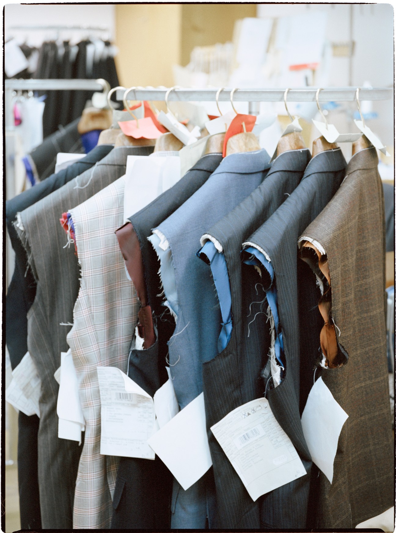 Regent suit samples in various colors hanging on a rail with white barcode labels and orange tags.