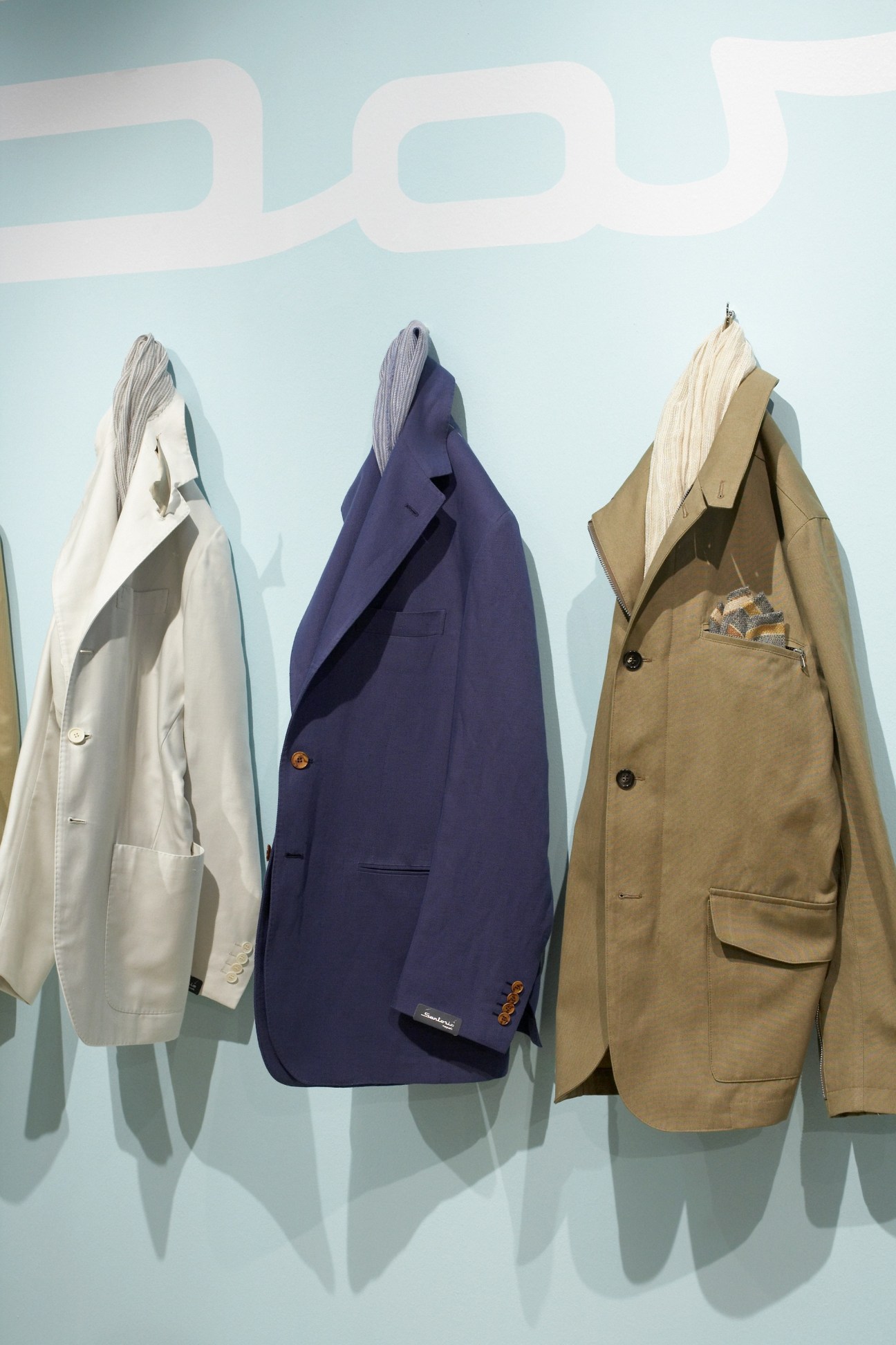 Three unstructured blazers by Sartorio displayed on mannequins against a light blue wall.