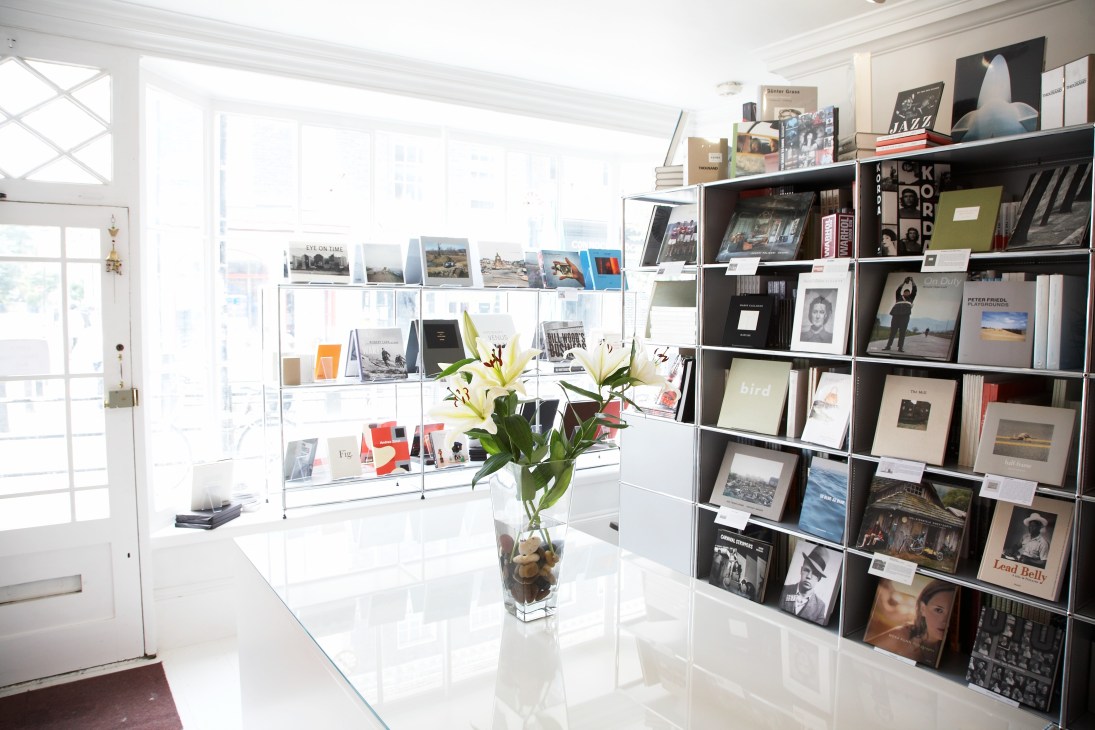 Interior of Steidville bookstore with white display cases, black shelving, and a vase of yellow flowers.