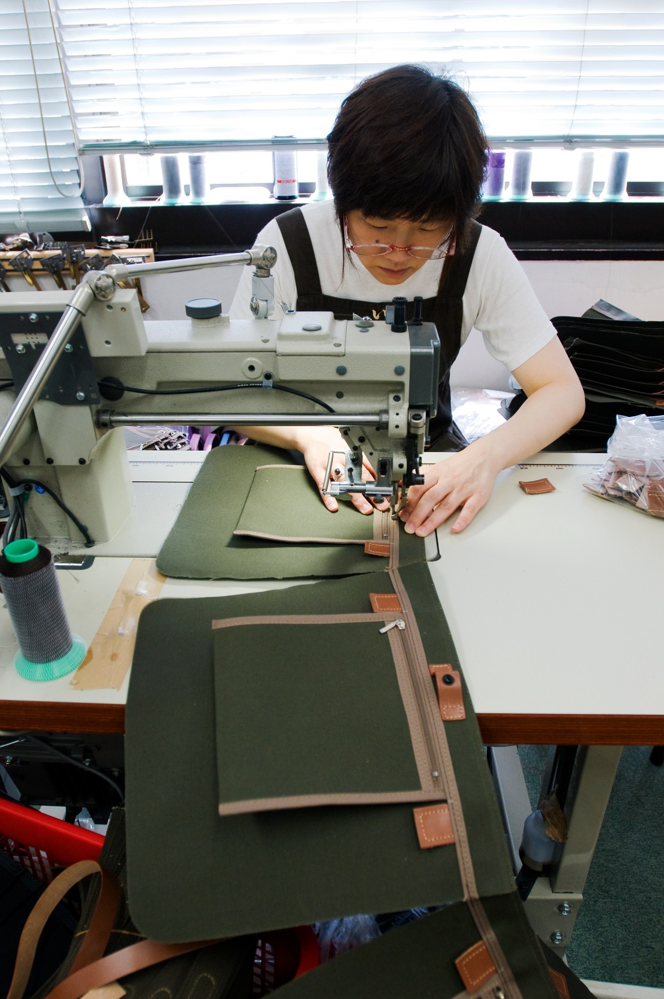 A machinist sews leather straps onto a green canvas bag at an industrial sewing machine in the Inujirushi workshop.