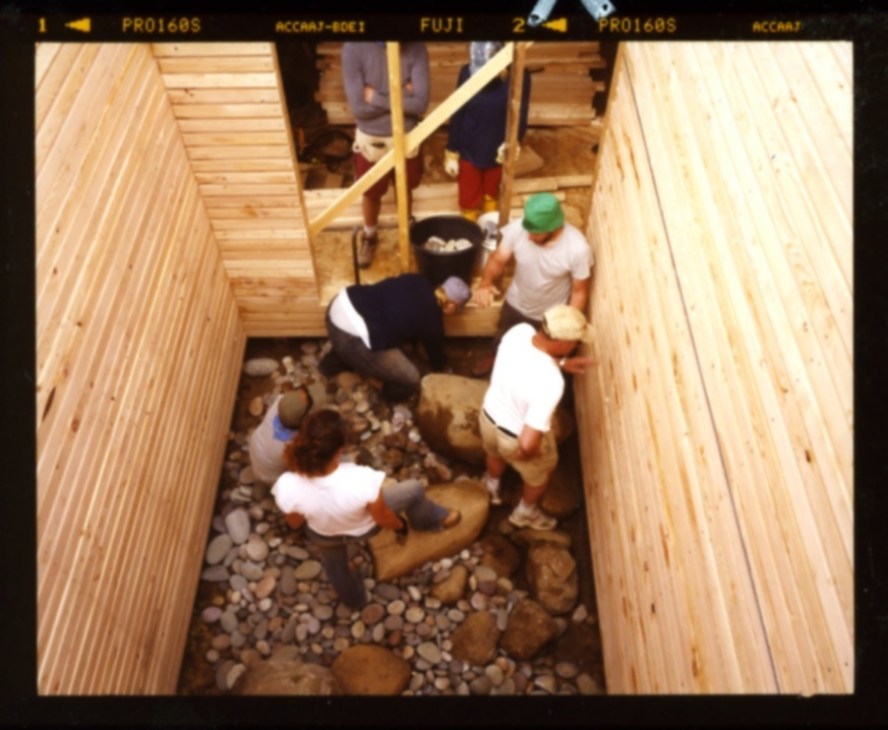 Overhead view of people standing in a wooden-framed interior space filled with smooth rocks and pebbles.