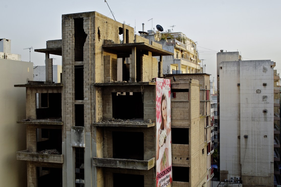Abandoned concrete building with empty windows and a fashion advertisement banner on Avenue de l'Indépendance in Beirut.
