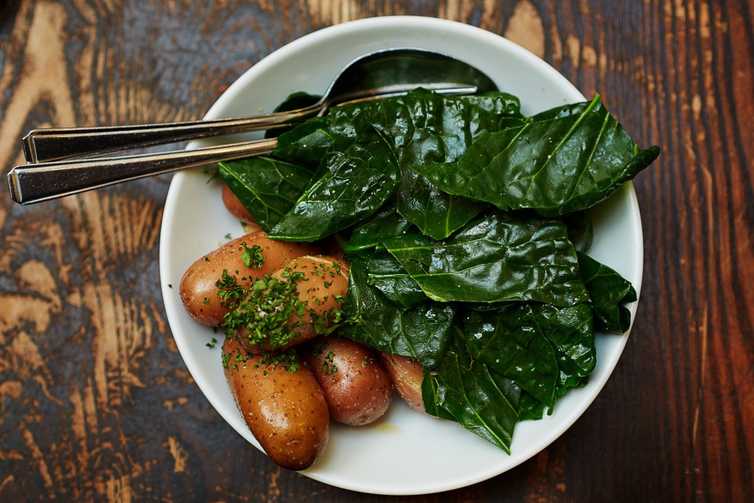Sprout tops and new potatoes served on a white plate with fork on wooden surface.