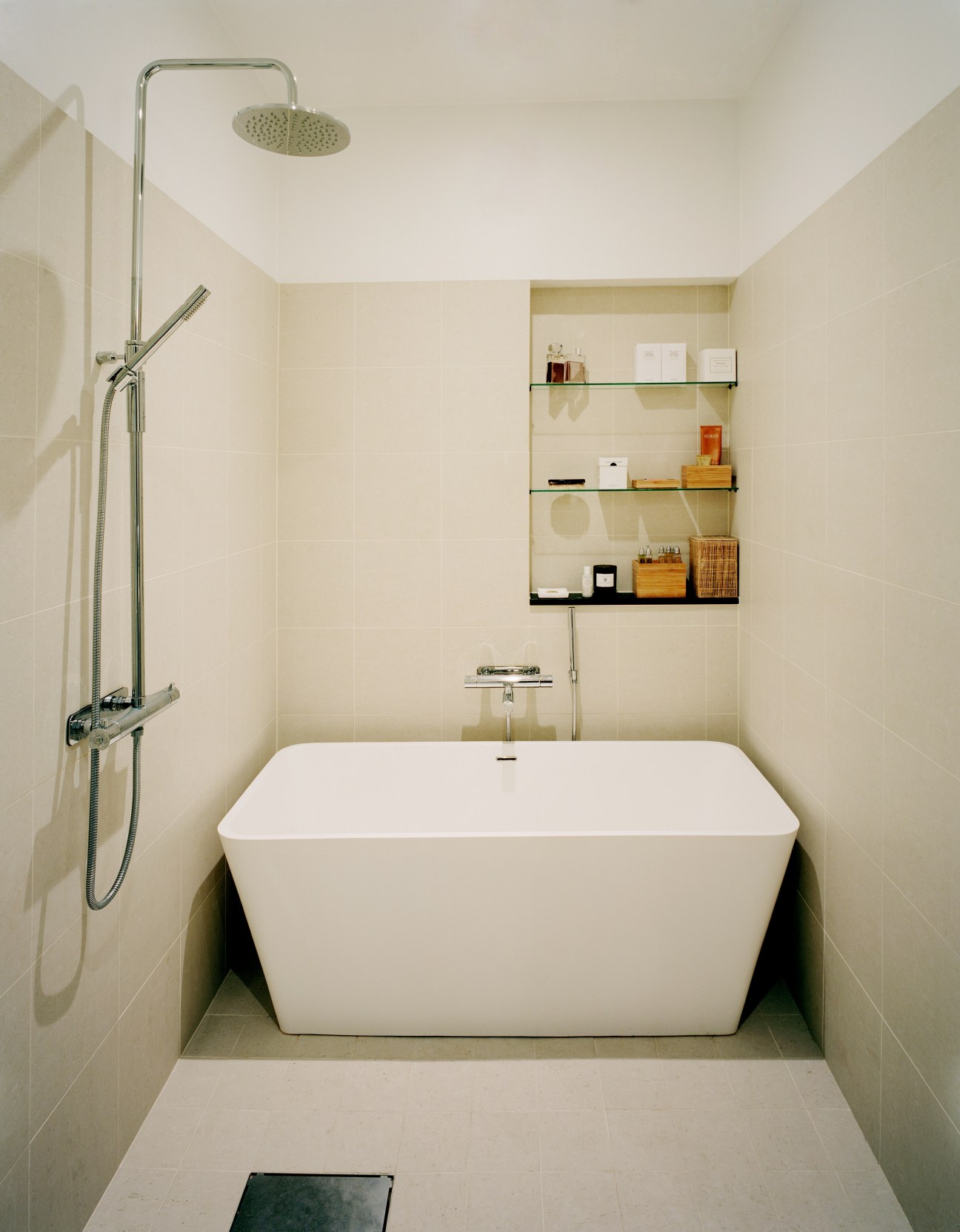 Minimalist bathroom with white freestanding tub, rainfall showerhead, and built-in shelving.