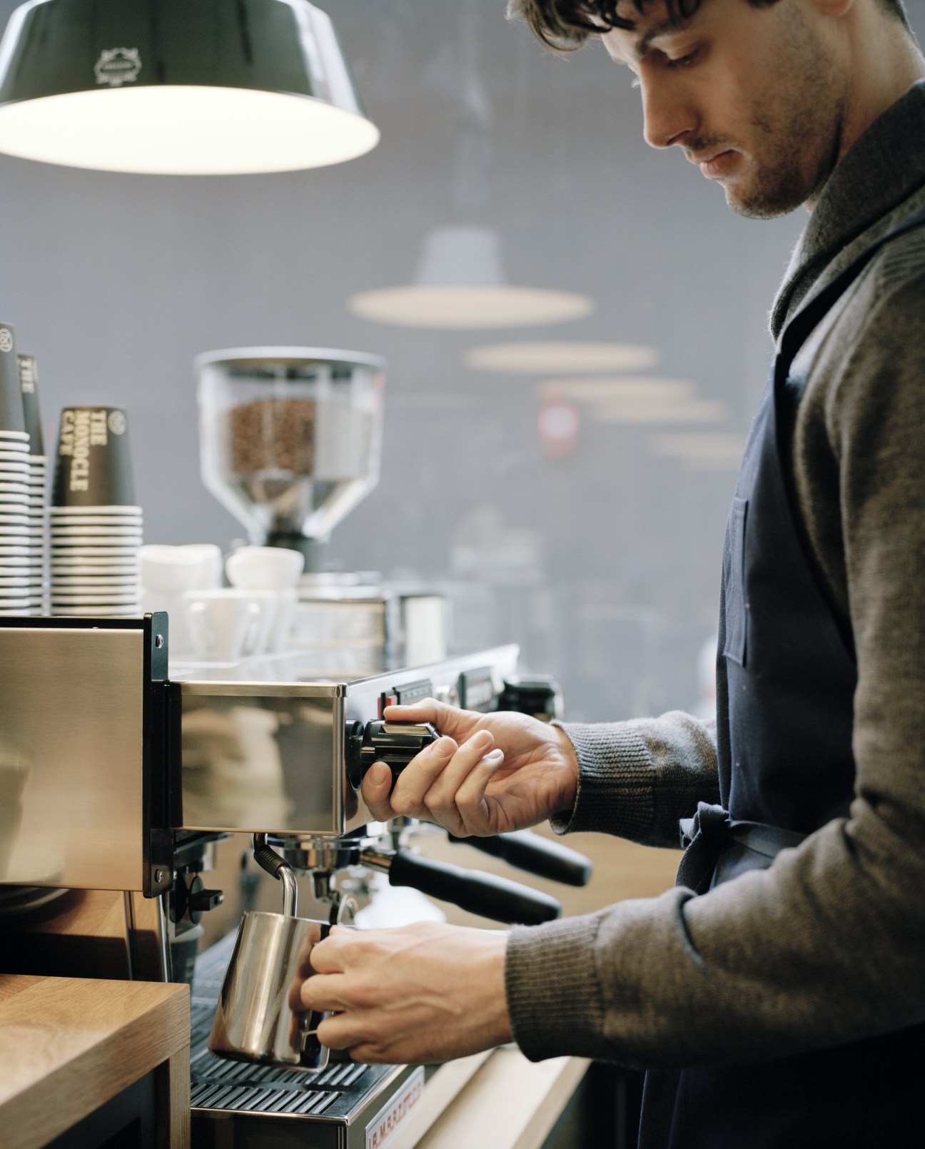 Barista using Allpress espresso machine to prepare coffee at Monocle Café counter.