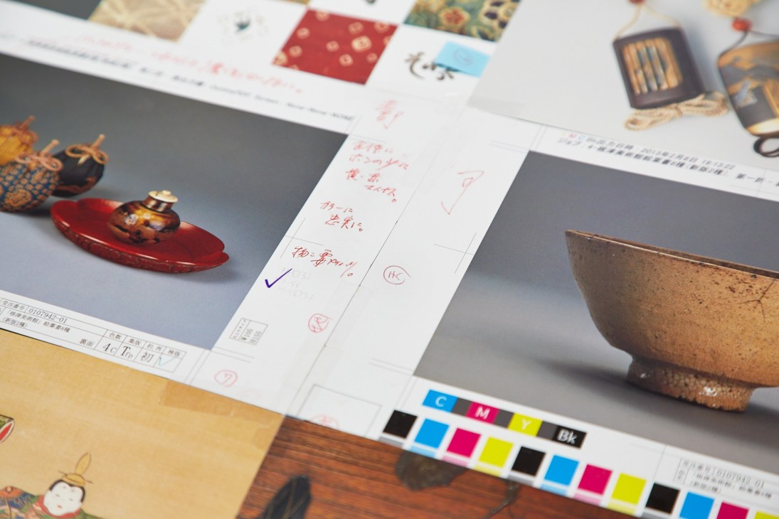 Color proofs for postcards with Japanese tea artifacts and handwritten annotations displayed on a printing table.