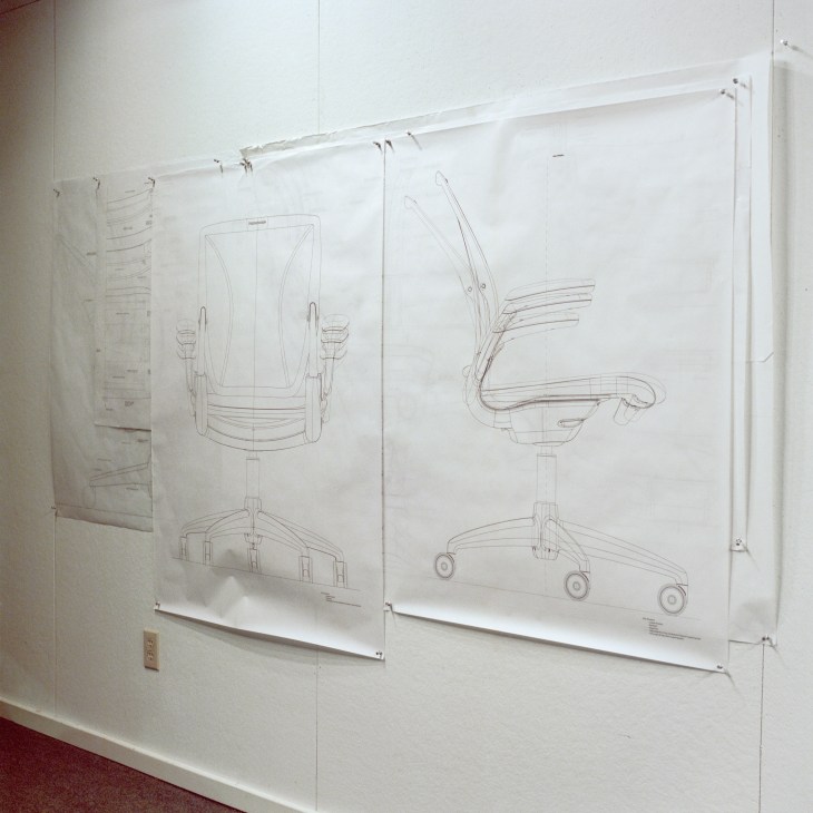 Technical drawings of office chair designs pinned to white boards on a studio wall.