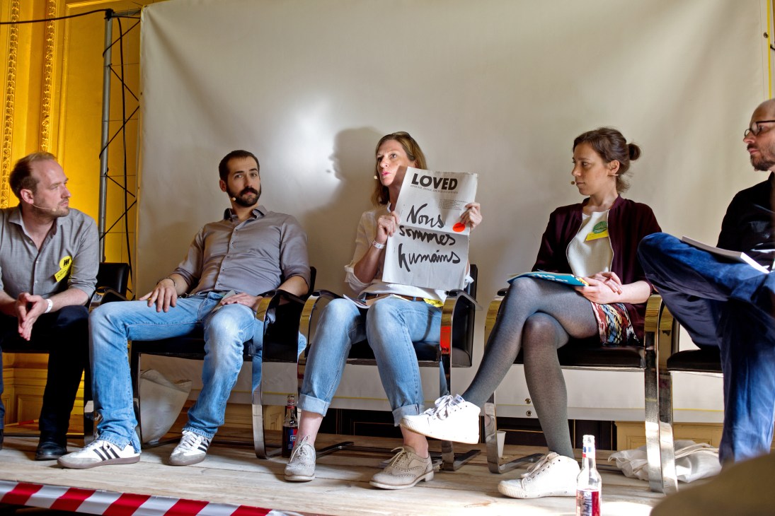 Panel discussion at Indiecon with five speakers seated, one woman holding a magazine with text about humanity.