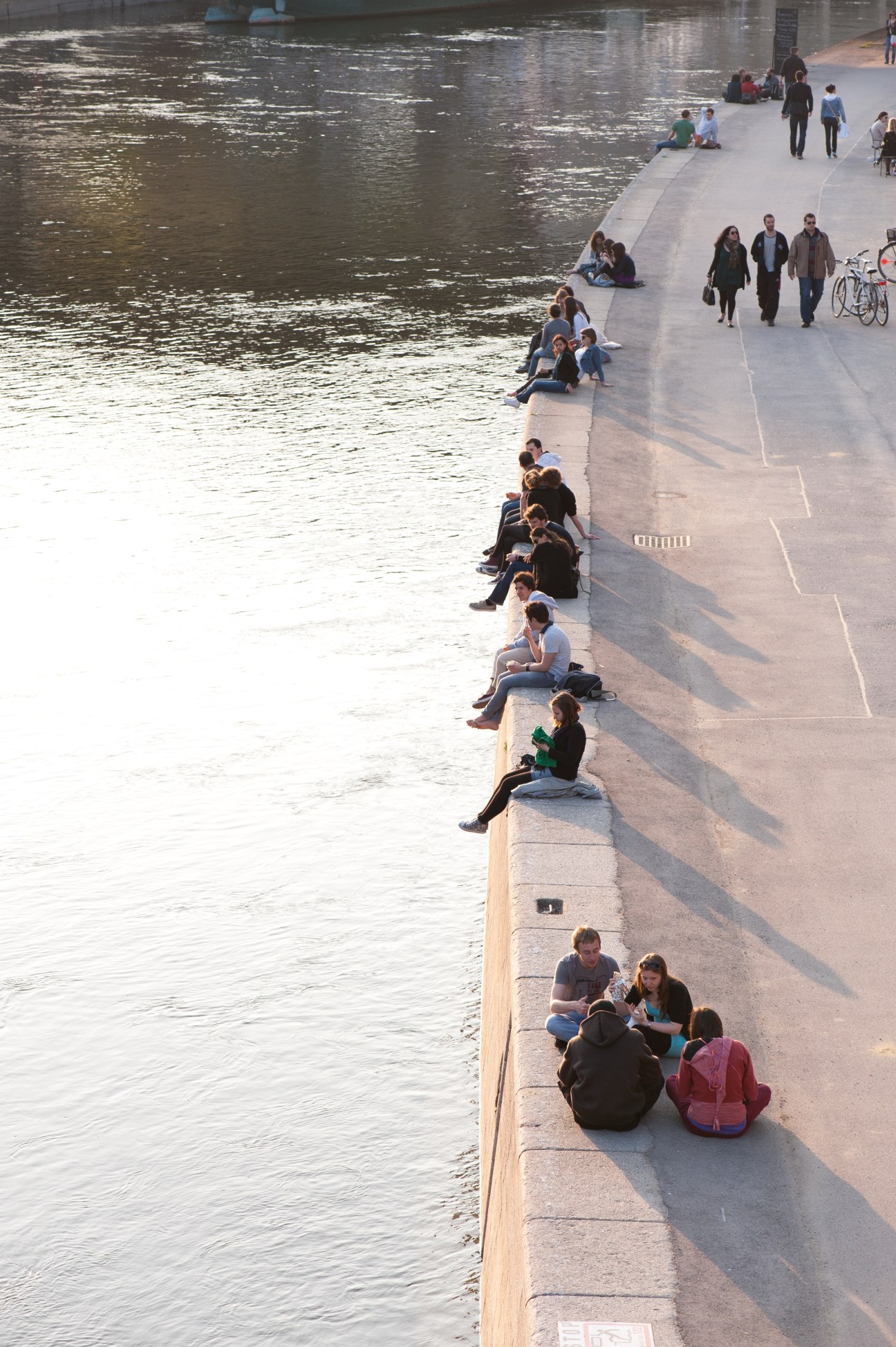 People sitting and walking along a canal waterfront promenade in Vienna.