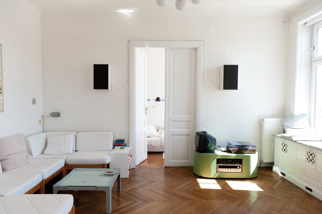 Minimalist living room with white walls, wooden herringbone floors, mid-century furniture and green accent table.