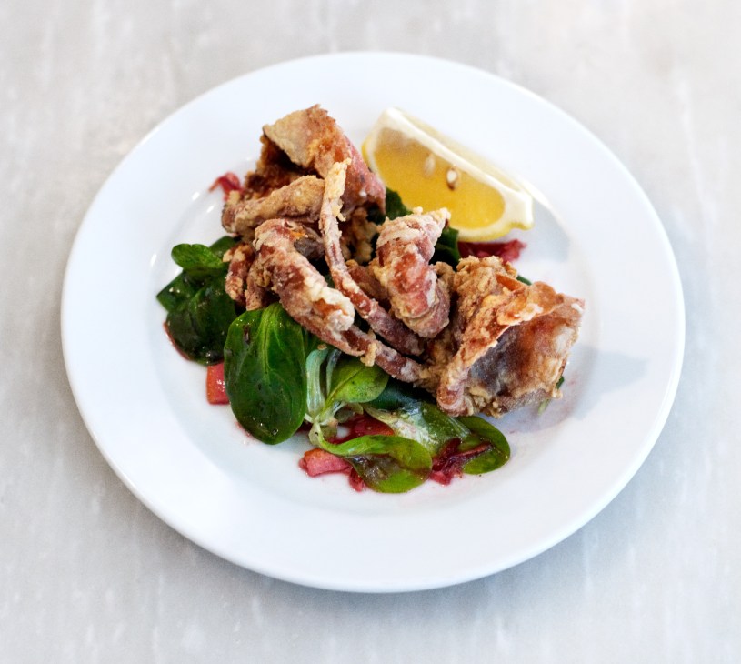 Fried soft-shell crab with blood orange and lamb's lettuce on a white plate with lemon wedge.