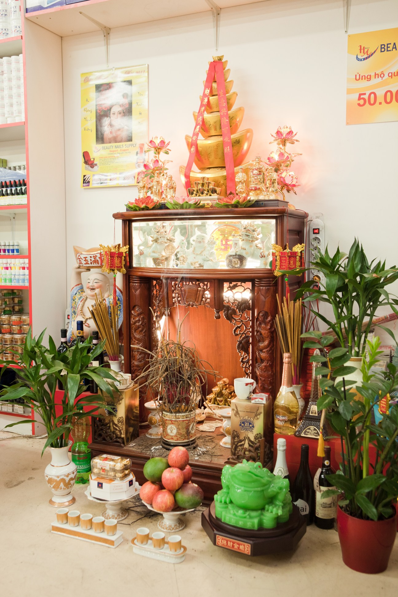 Buddhist shrine with golden tiered structure, red ribbons, fresh fruit offerings, incense, and decorative figurines in a retail store.