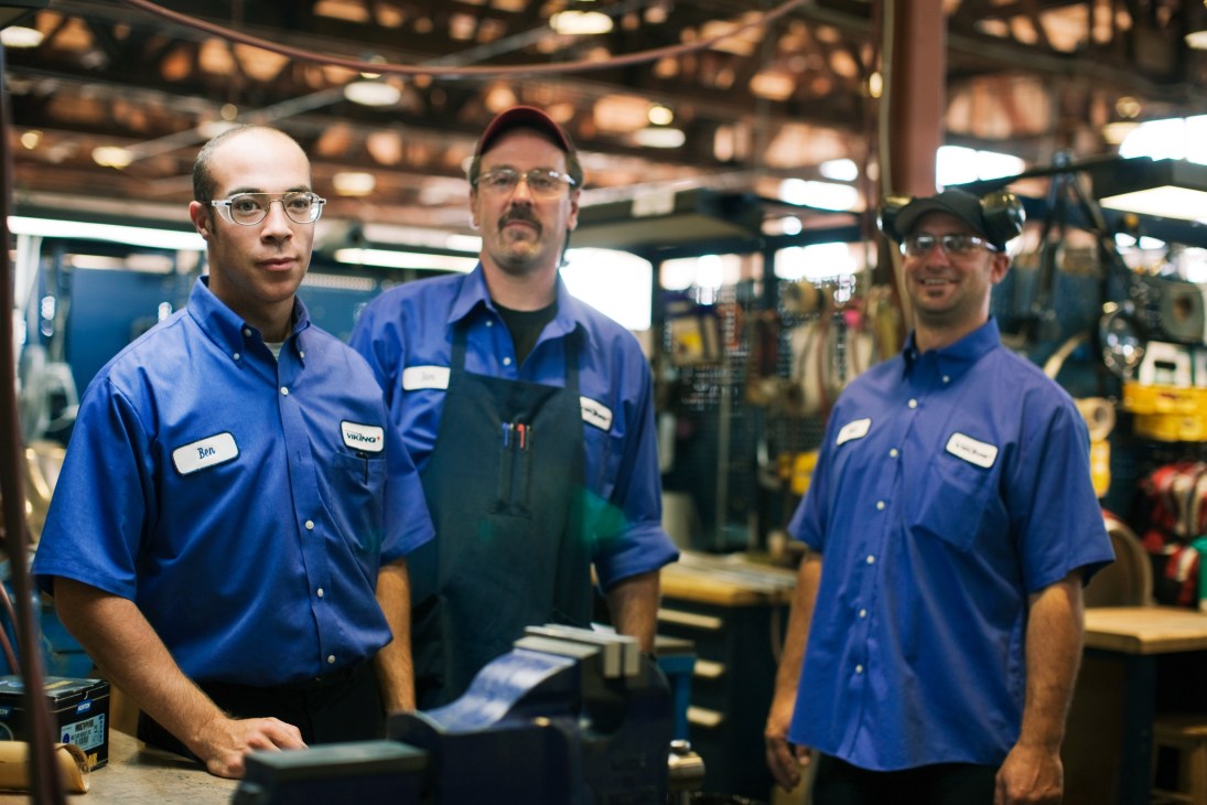 Three Viking Air factory workers in blue uniforms stand in an aircraft assembly hangar.