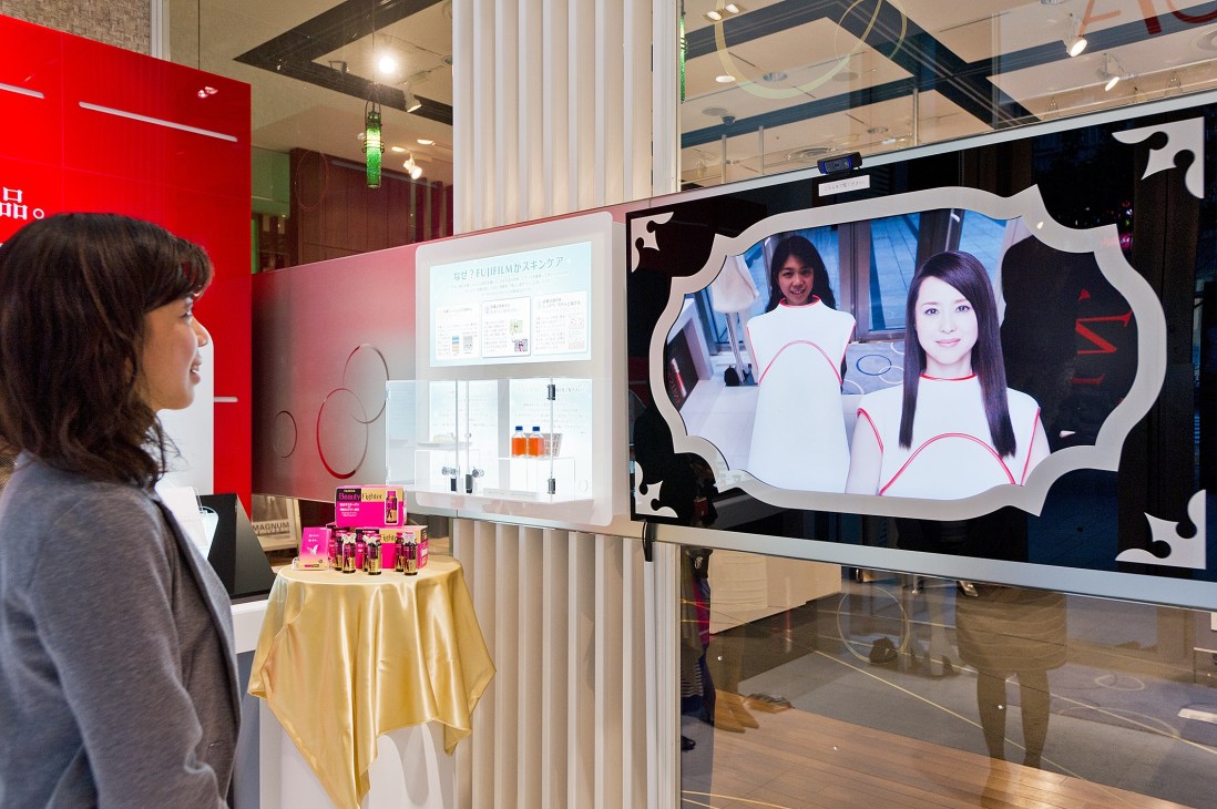 Woman viewing interactive Astalift advertisement display at beauty counter in Tokyo retail space.
