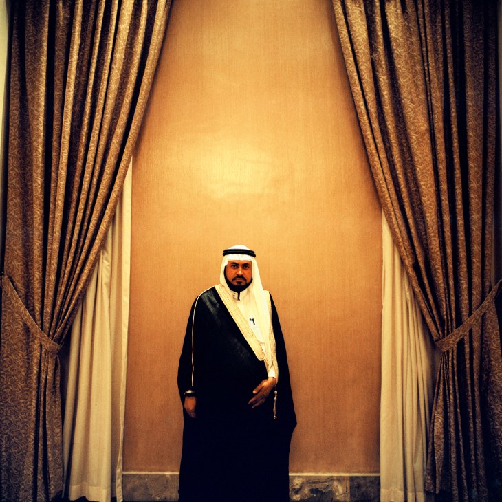 Man in traditional Arab dress standing between gold curtains in an elegant interior.