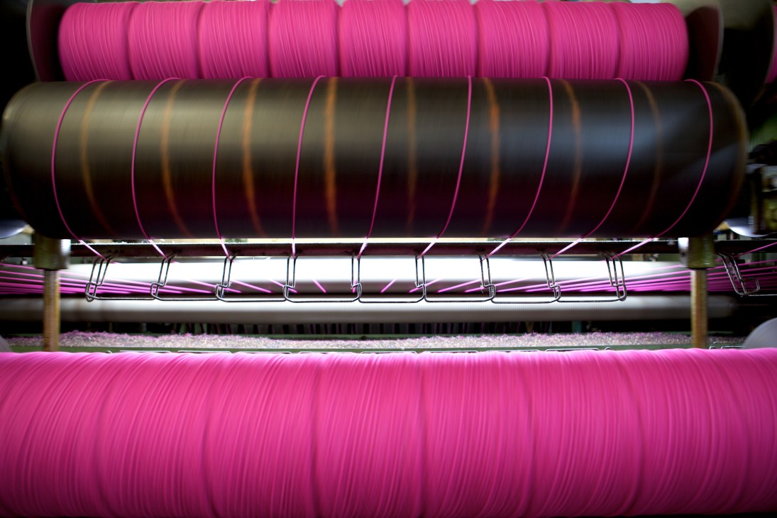 Spools of brightly dyed pink and dark wool yarn wound on machinery used in Harris Tweed production.