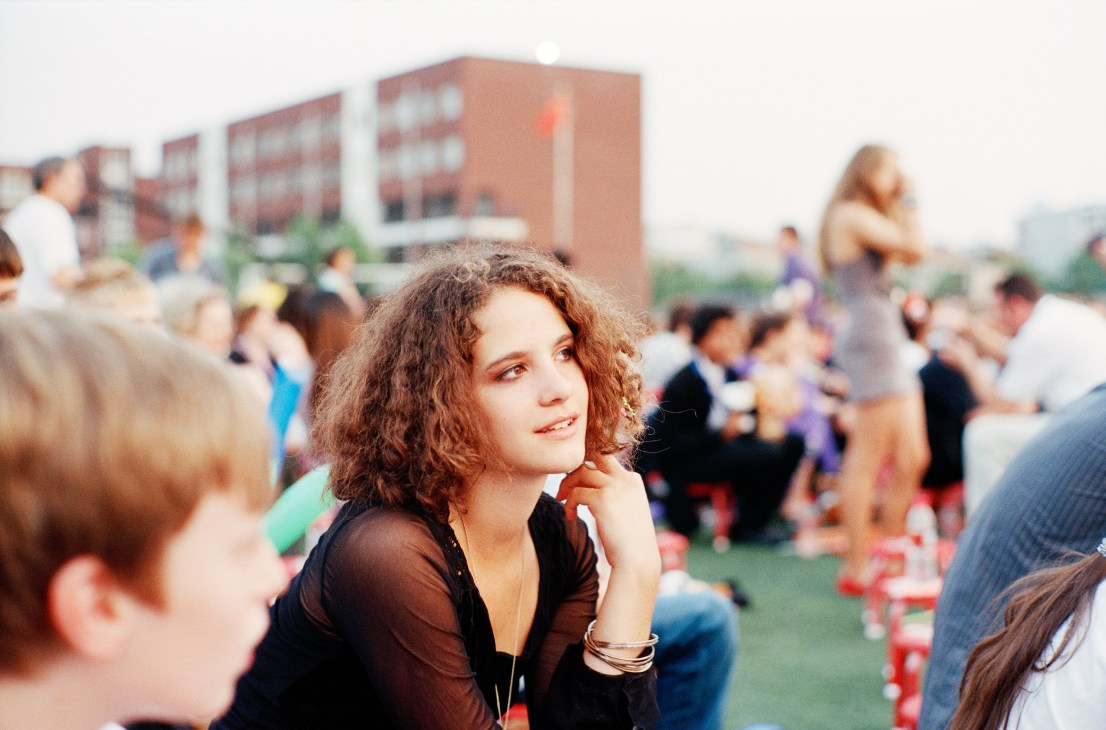 A young woman with curly reddish-brown hair sits among other students at an outdoor event in China.