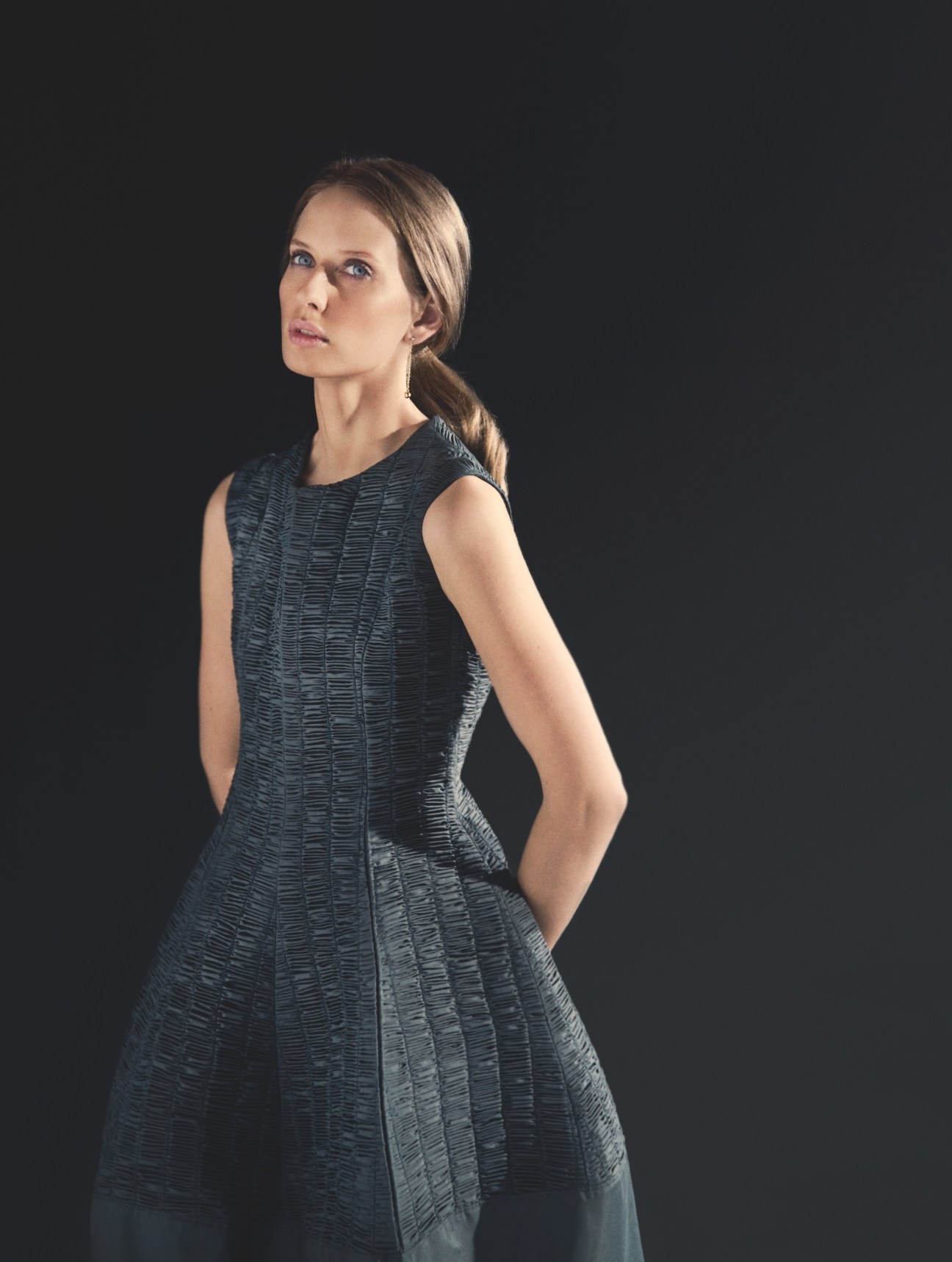 Model wearing Dior dress with Trussardi 1911 bag and Cartier bracelet against dark background.