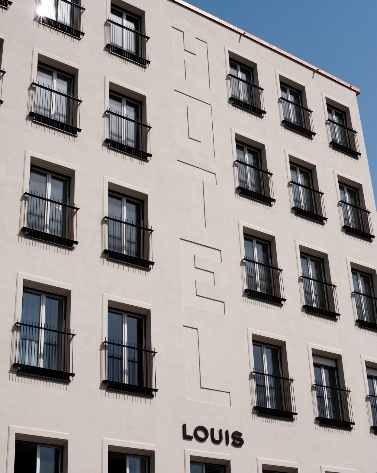 Exterior facade of the Louis Hotel in Munich with cream-coloured walls, black wrought-iron balconies and the hotel name displayed at street level.