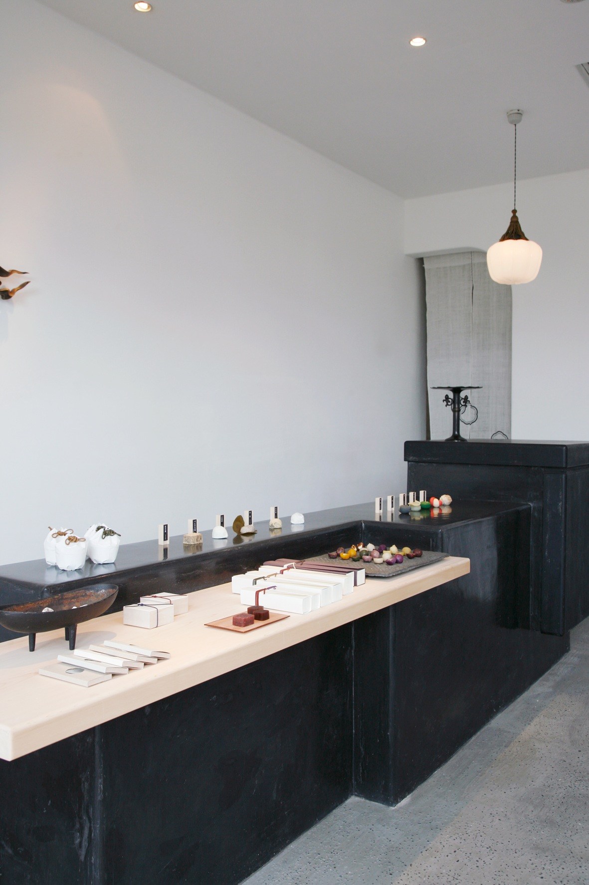 Interior of Baishinka tea house in Tokyo displaying traditional sweets and products on black counter with pendant lighting.