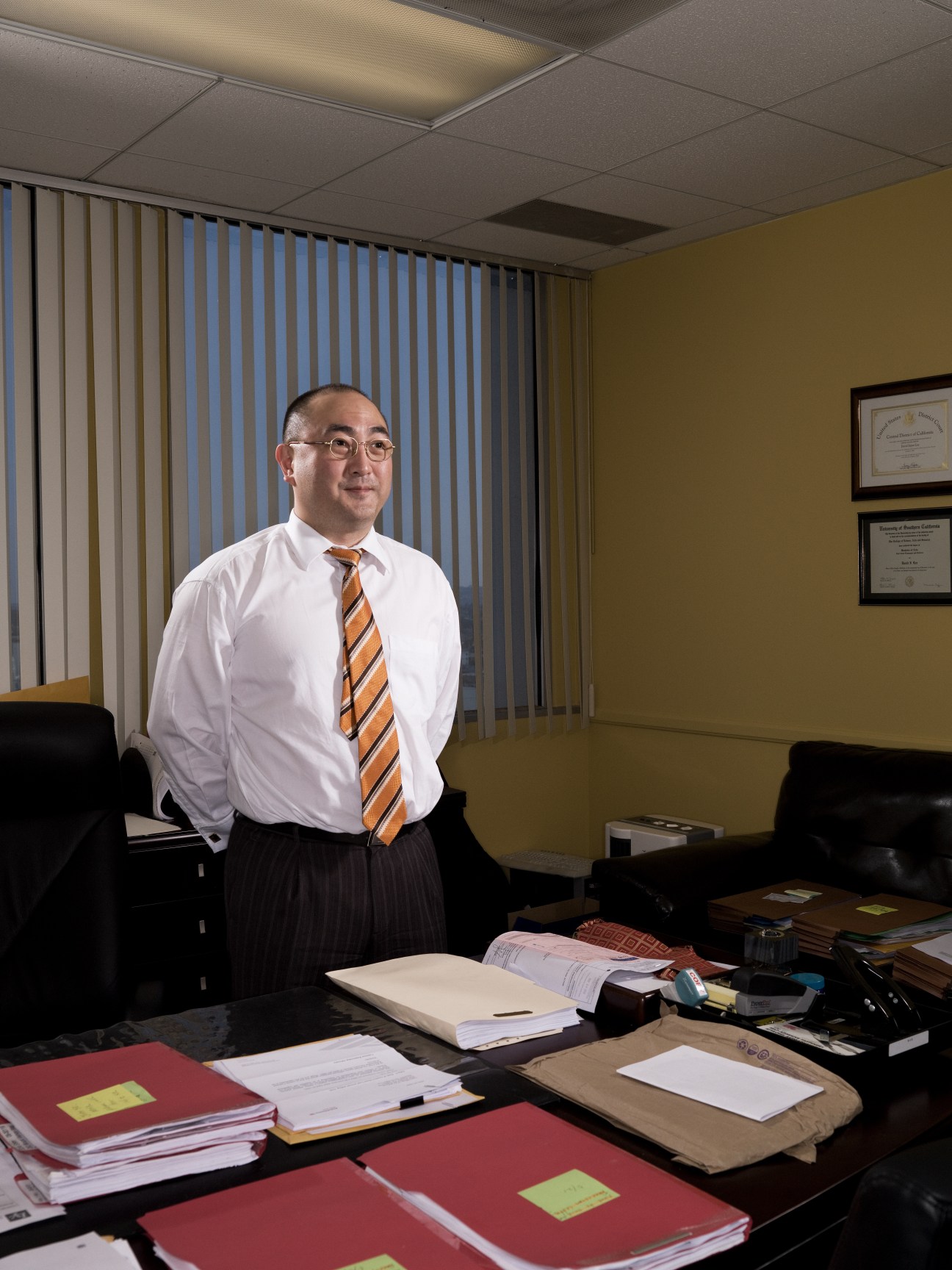 David Inpyo Lee, an immigration lawyer, stands in his office beside his desk with documents and files.