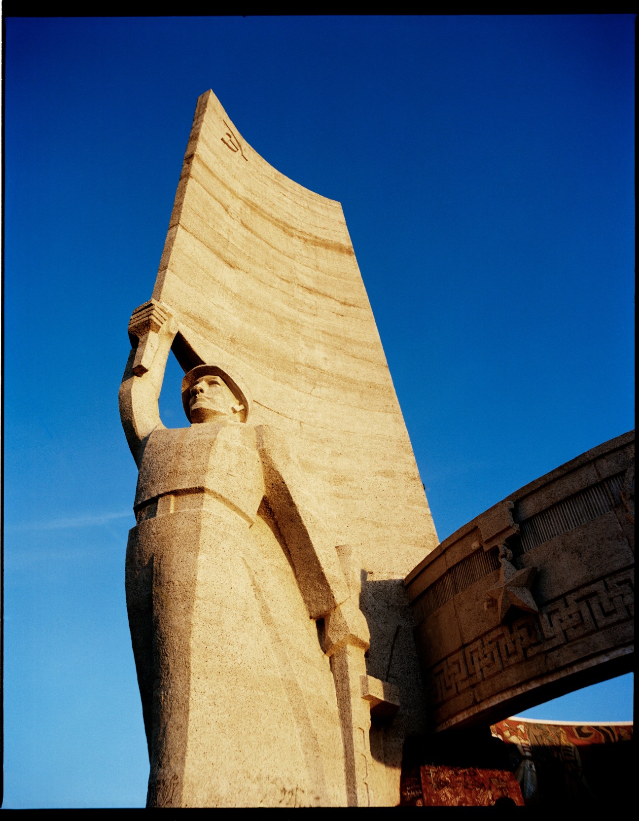 Zaisan Memorial stone statue holding torch against blue sky with monument tower behind it in Ulan Bator, Mongolia.