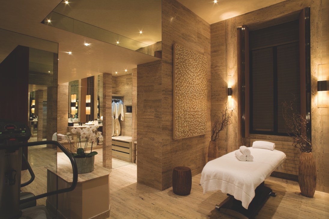 Spa suite with massage table, marble walls, and bathroom with mirrors at The Park Hyatt Milan.
