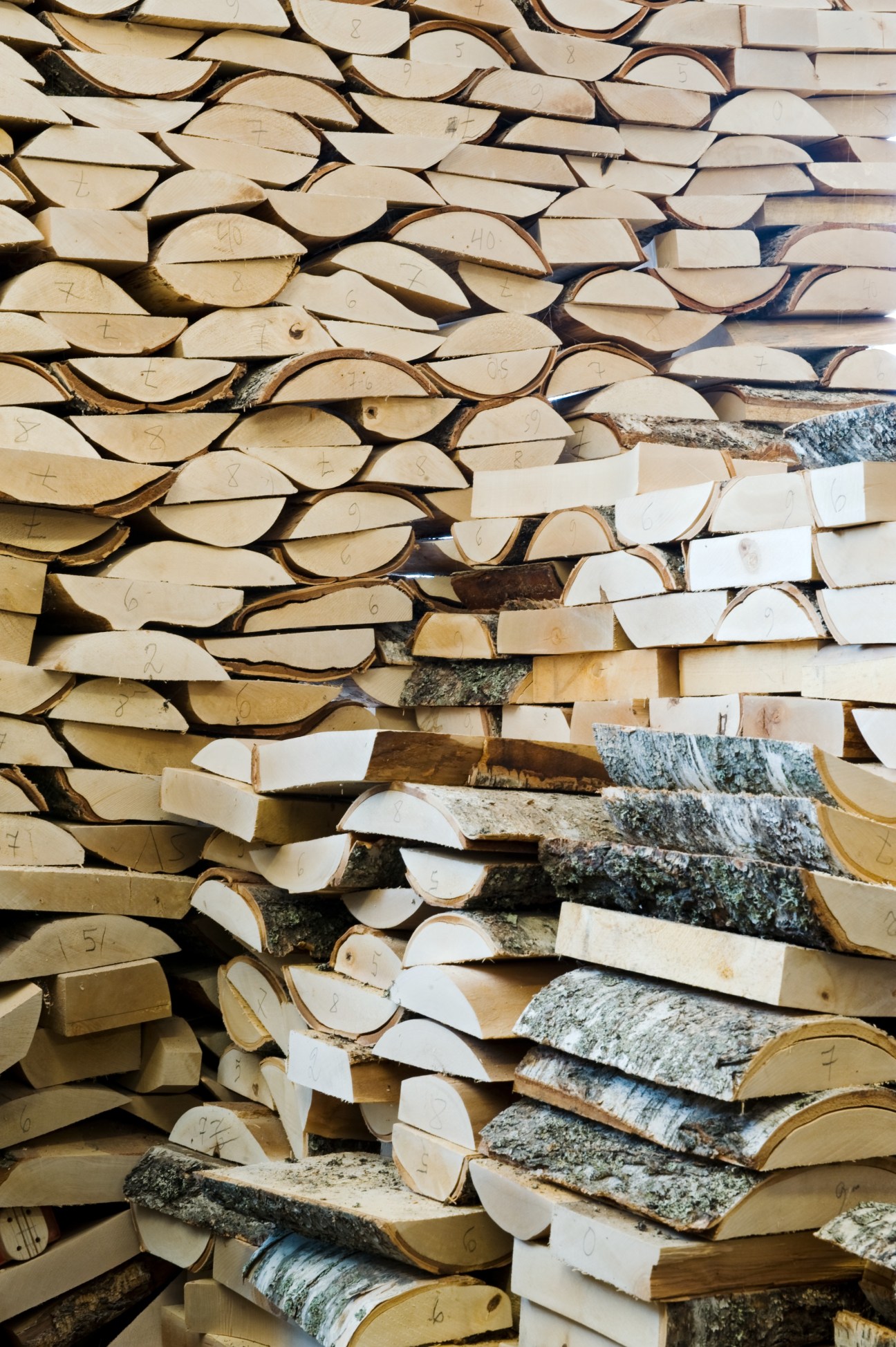 Wooden clog soles stacked in rows, showing birch and ash wood with bark and numbered markings.