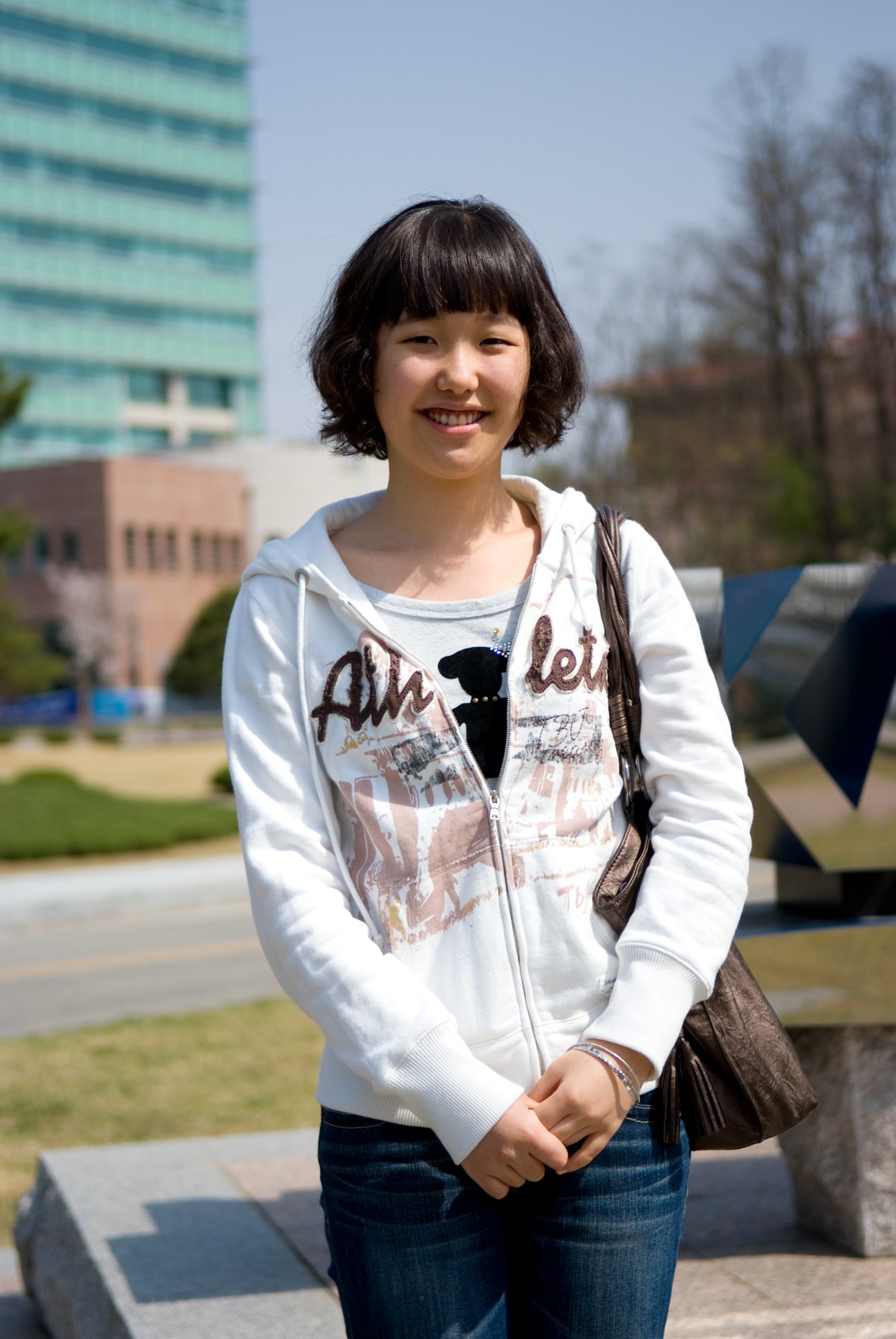 Biology undergraduate A Young Kwak smiles at the KAIST campus with modern buildings in the background.