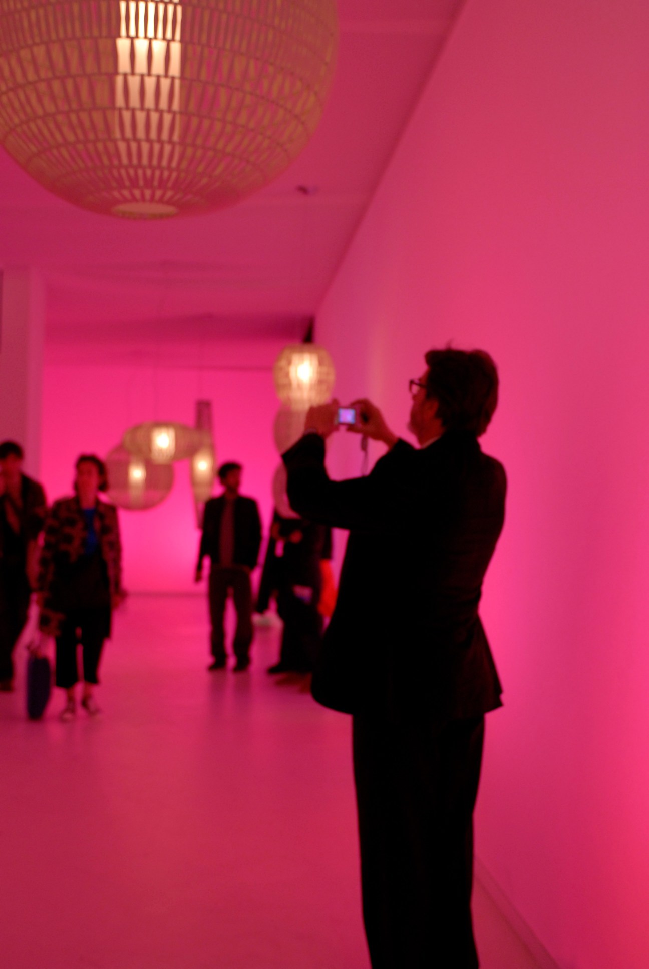 Visitors photograph pendant lights at the Foscarini stand with bright pink walls and ambient lighting.