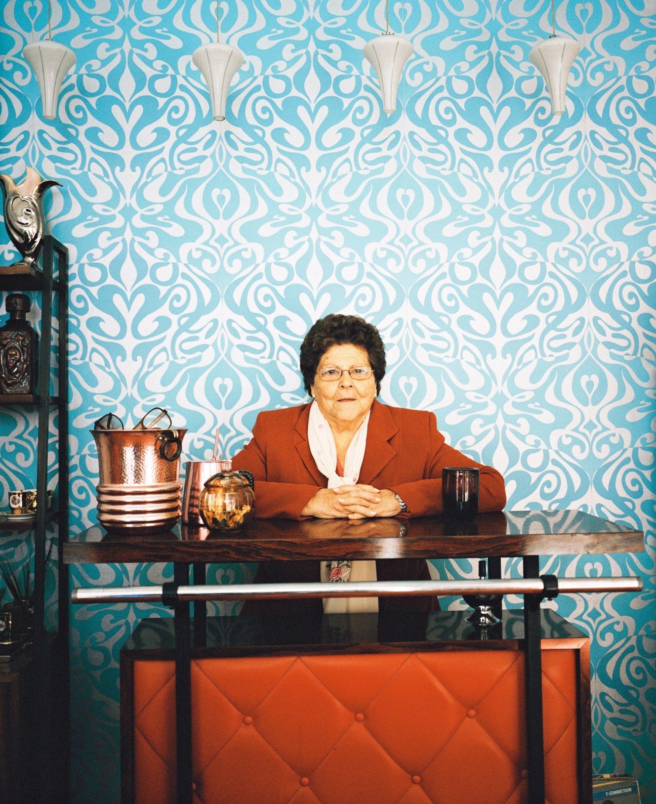 Woman in red blazer sitting at table against turquoise patterned wallpaper in Arsenico store.