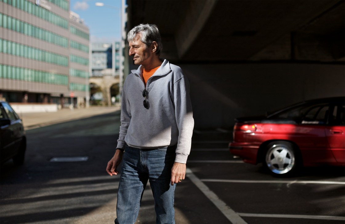 Dentist Theo Roetheli stands beside his rare red Subaru SVX '93 in an urban parking area.