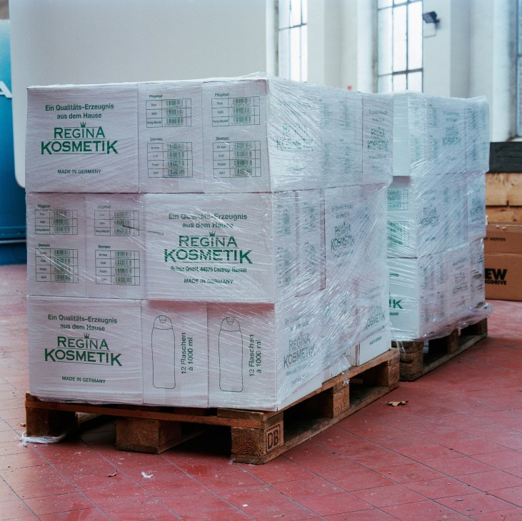 Two wrapped pallets of Regina Kosmetik cosmetics on a wooden base in an industrial warehouse.