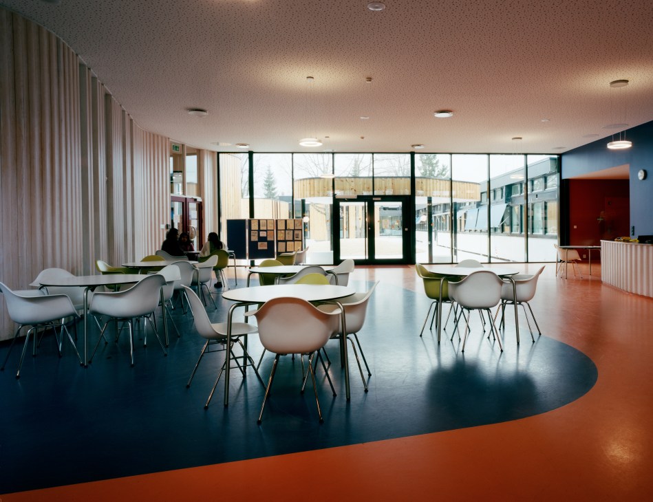 Oslo International School's new lobby with Vitra chairs, curved seating areas, orange rubber flooring and large windows overlooking the courtyard.